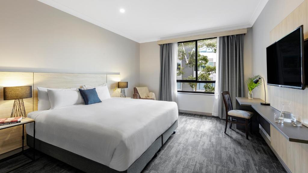 um quarto de hotel com uma cama grande e uma janela em Oaks Sydney North Ryde Suites em Sydney