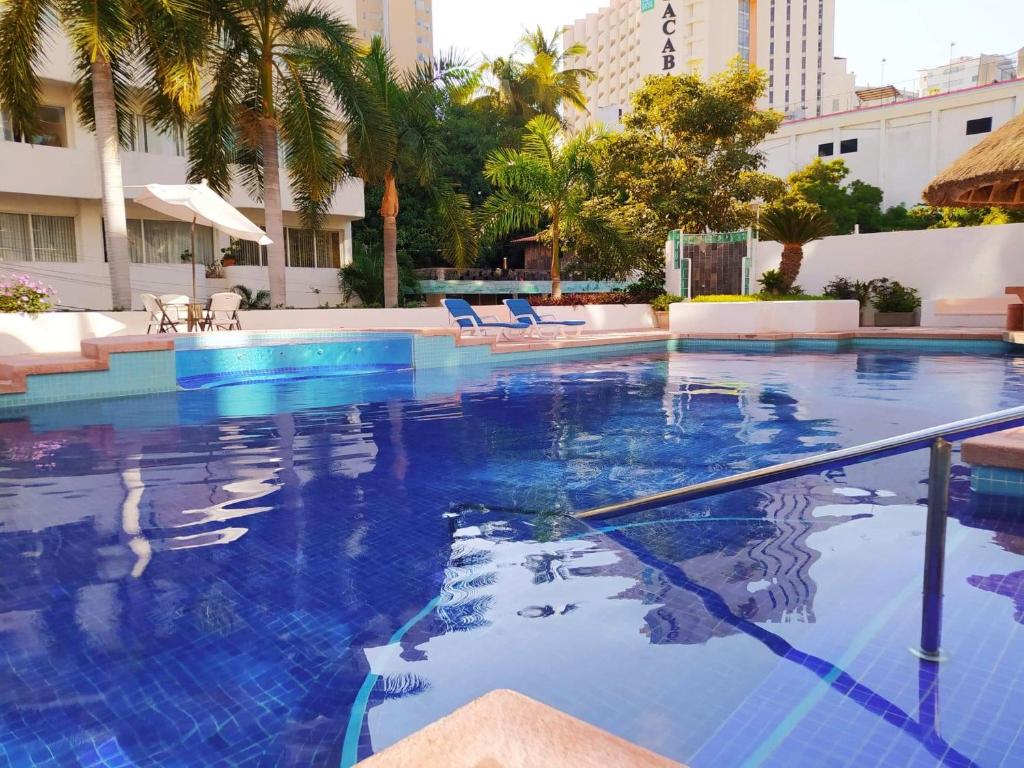 a large swimming pool with blue water and palm trees at Espléndido departamento en Acapulco in Acapulco
