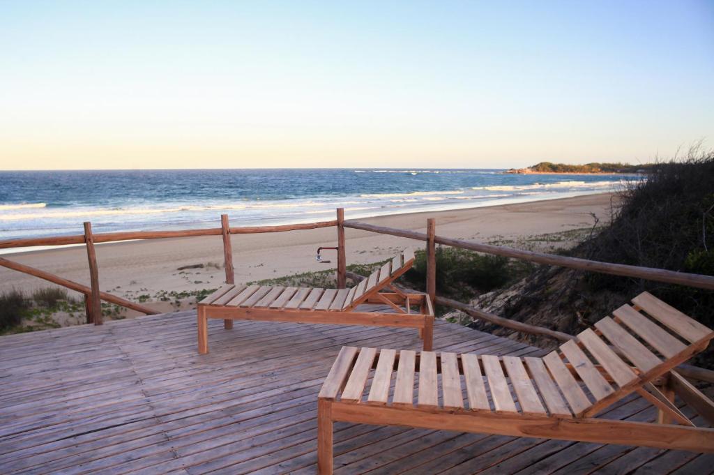 dois bancos sentados num passeio de madeira junto à praia em Musica do Mar Beach Front Apartments, Ocean View em Praia do Tofo