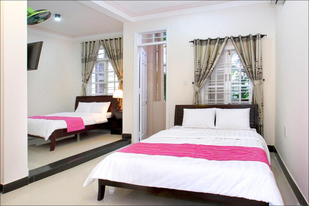 2 camas en una habitación con paredes y ventanas blancas en Cosy House Homestay, en Hoi An