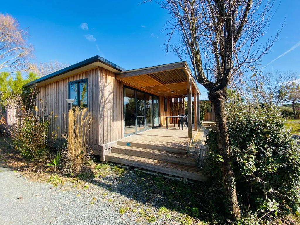 a small house with a wooden porch and a tree at Camping Paradis 4 étoiles A La Corniche La Rochelle Angoulins in Angoulins-sur-Mer