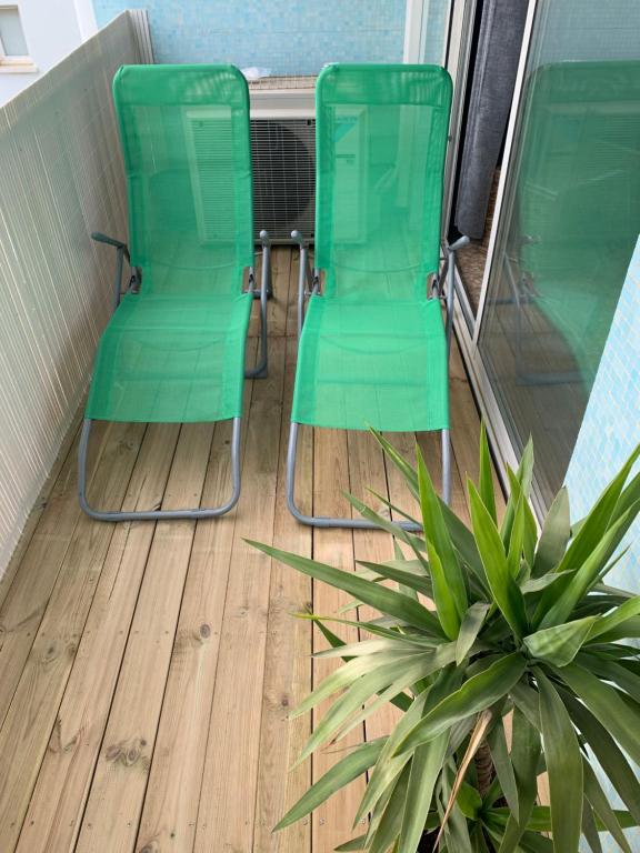 - deux chaises vertes sur une terrasse couverte avec une plante dans l'établissement Canet Plage Appartement Cosy très calme, à Canet