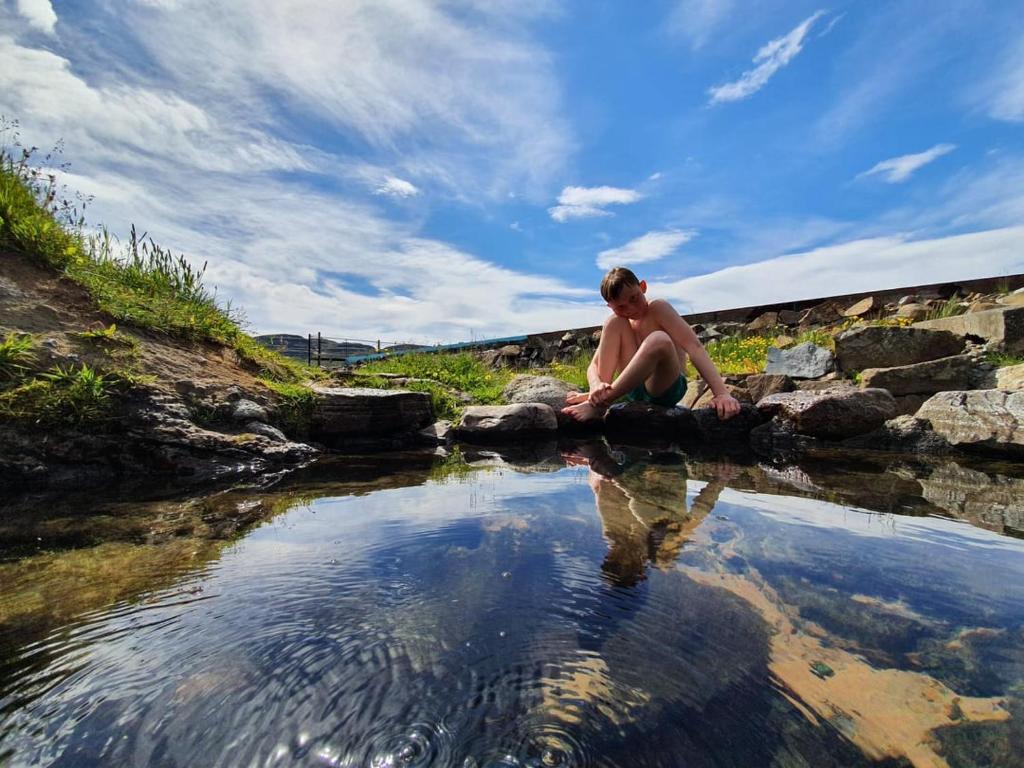 un hombre sentado en las rocas cerca de un cuerpo de agua en Hótel Laugarhóll with natural hot spring, en Hólmavík
