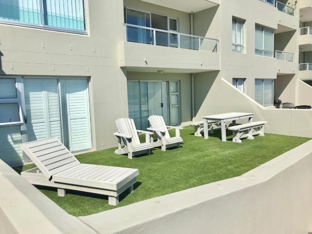 a patio with lawn chairs and a table and a building at Voir la Mer - Blouberg Beach in Bloubergstrand