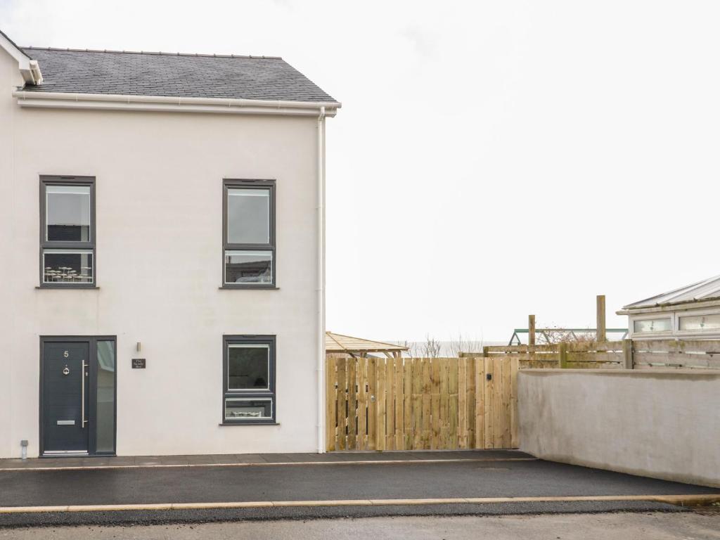 a white house with black windows and a wooden fence at The Sandy Bee in Benllech
