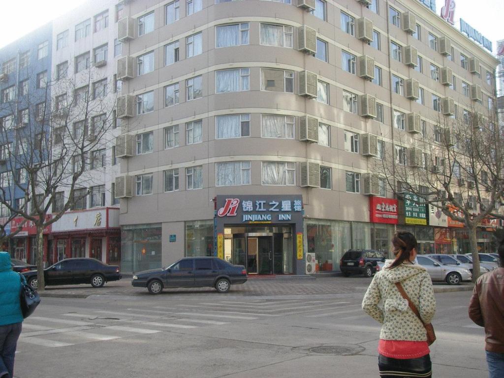 een vrouw die in een straat voor een gebouw loopt bij Jinjiang Inn - Qingdao Xiangjiang Road in Huangdao