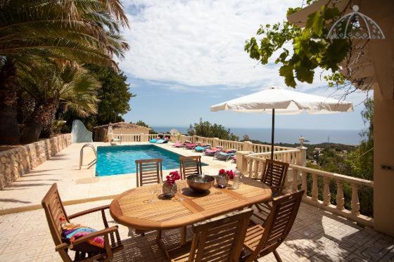 einem Holztisch mit Stühlen und einem Sonnenschirm neben einem Pool in der Unterkunft Splendid in Altea