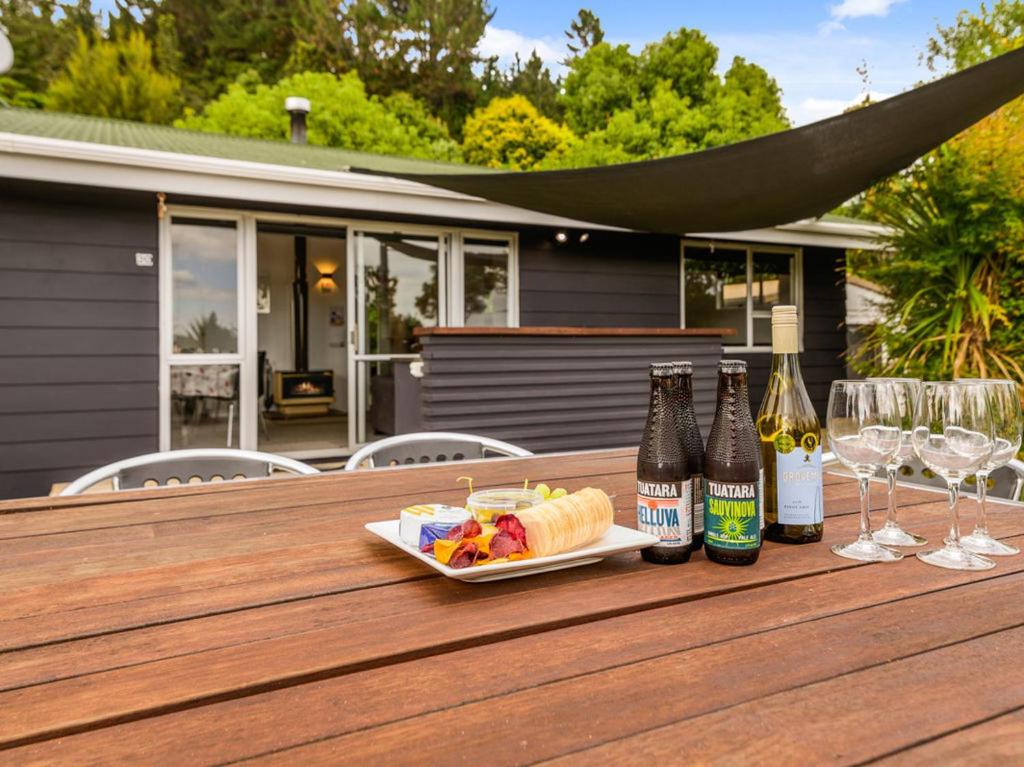 einen Tisch mit einem Teller Essen und zwei Flaschen Wein in der Unterkunft Fantail Cottage - Lake Rotoiti Holiday Home in Rotoiti