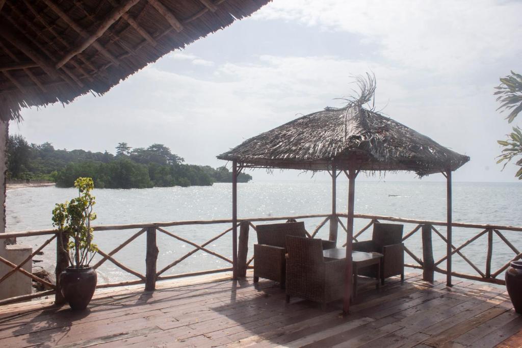 a deck with chairs and a straw umbrella on the water at Sea View Beach Hotel in Zanzibar City