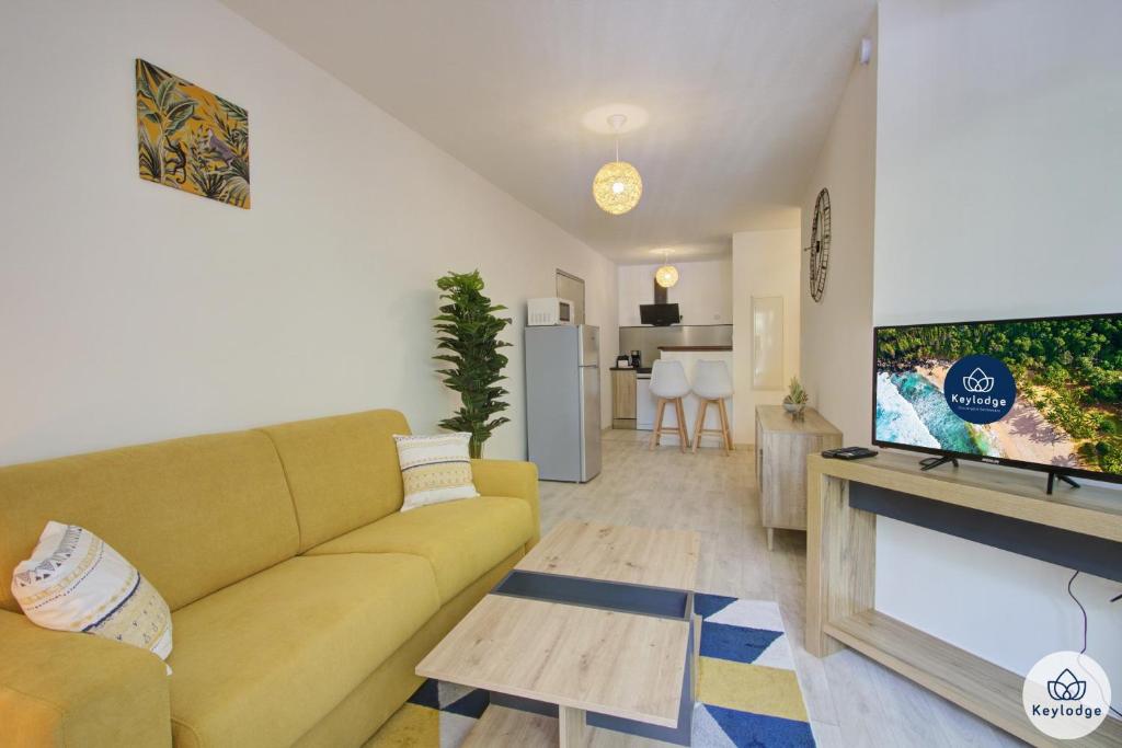 een woonkamer met een gele bank en een flatscreen-tv bij T2 - Fiorella - Piscine et terrasse - 36m2 - Saint-Denis in Sainte-Clotilde