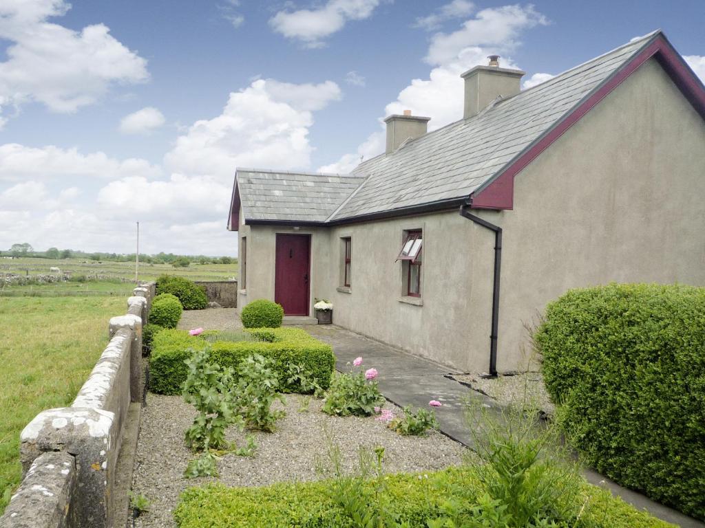 a small white house with a red door and some bushes at Cappacurry Lodge Ballinrobe in Ballinrobe