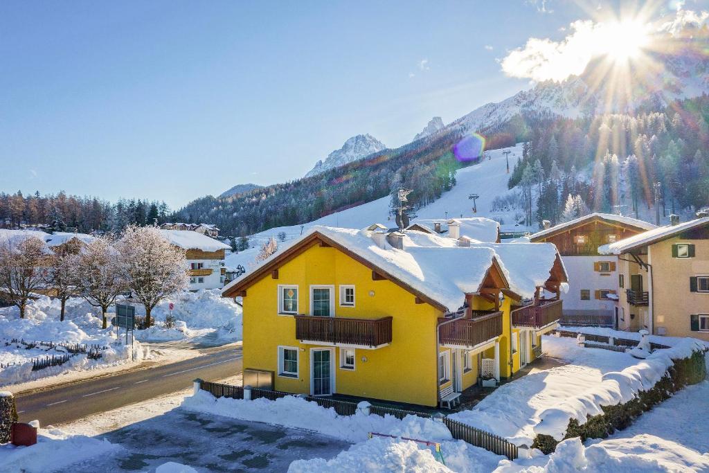 a yellow house in the snow with the sun behind it at Appartamenti Lercher Anna in San Candido