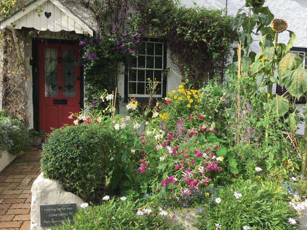 a garden in front of a house with a red door at Gardener's Cottage in Kingsbridge