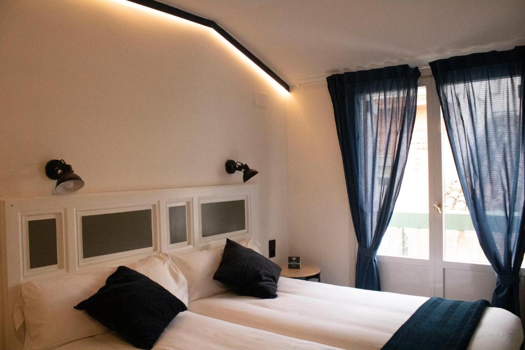 a bedroom with a white bed with black pillows and a window at Hotel Alda Jolio Jaca in Jaca