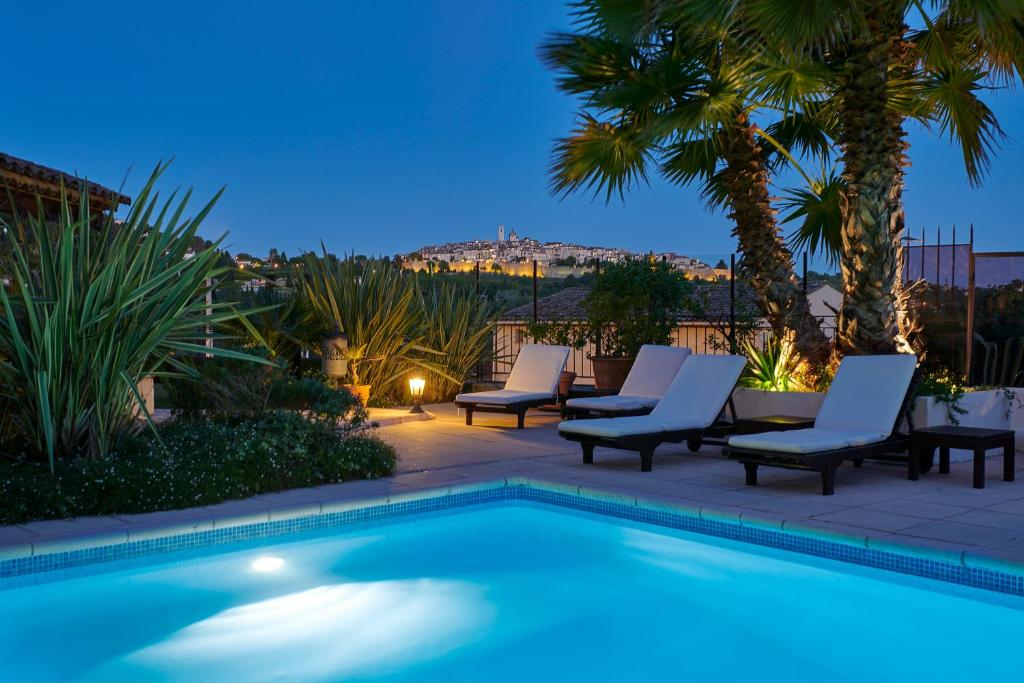 a swimming pool with chaise lounge chairs and palm trees at Hôtel La Grande Bastide in Saint-Paul-de-Vence
