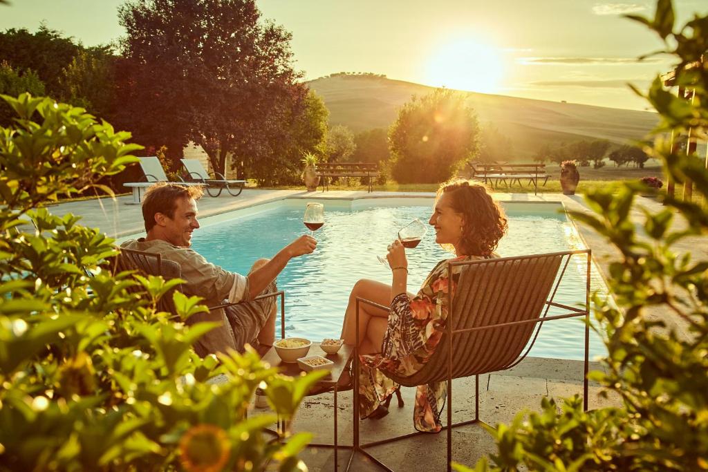mężczyzna i kobieta pijący wino przy basenie w obiekcie Agriturismo Lunadoro w mieście Monticchiello