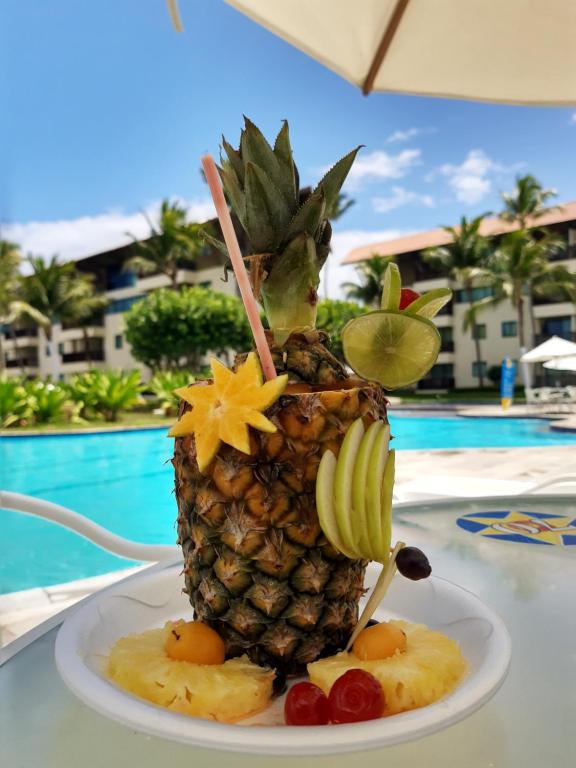 una piña en un plato junto a una piscina en Marulhos Resort Studio Master en Porto de Galinhas