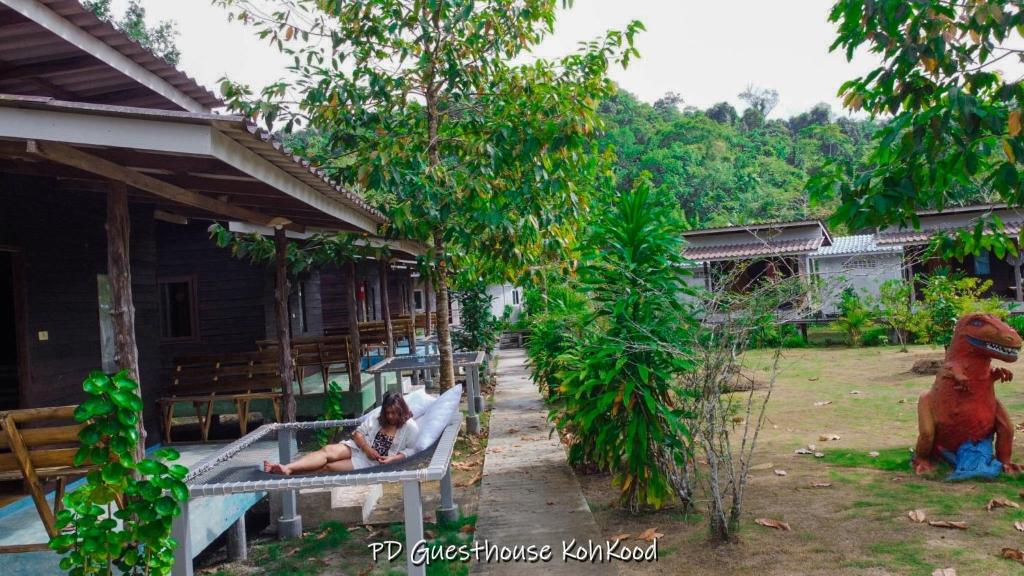 una mujer sentada en un banco junto a una casa en PD Guesthouse en Ko Kood