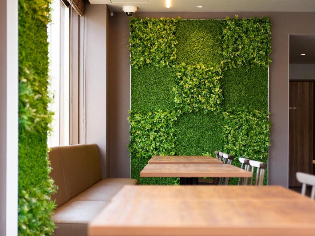 Super Hotel Kanku Kumatoriekimae في إيزوميسانو: جدار أخضر في مطعم مع طاولة خشبية