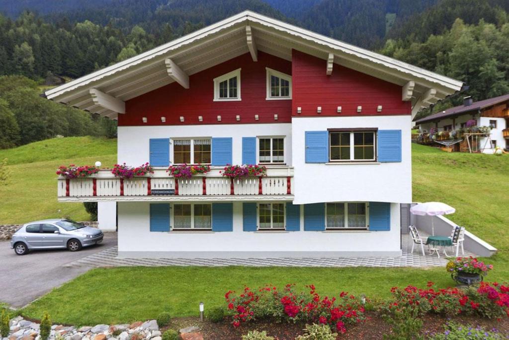 a red and white house with a balcony and a car at Ferienwohnung Erhard in Silbertal