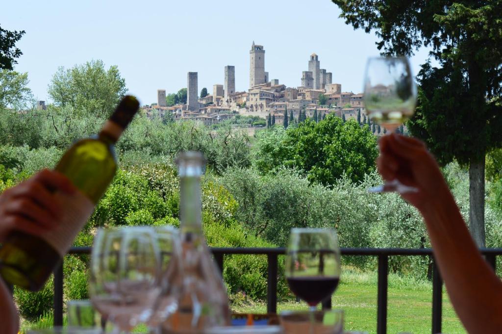 uma pessoa segurando copos de vinho com uma cidade ao fundo em Tenuta Guardastelle - Agriturismo and vineyard em San Gimignano