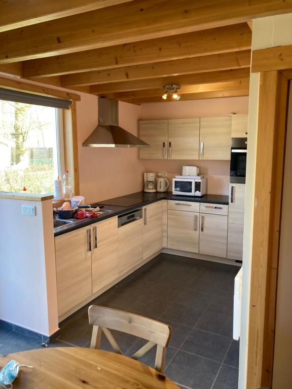 cocina con armarios de madera, mesa y microondas en Bungalow, en Froidchapelle