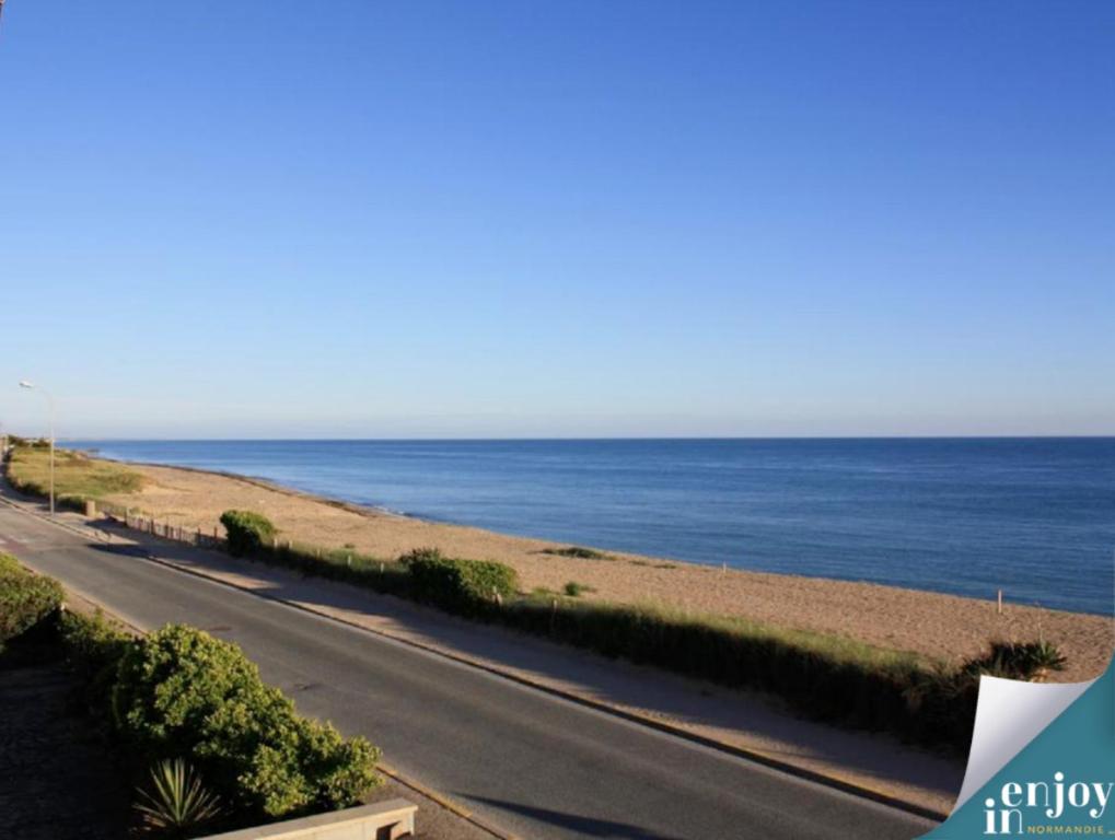 an empty road next to the ocean on a clear day at Villa Denise Petit Gîte in Barneville-Carteret