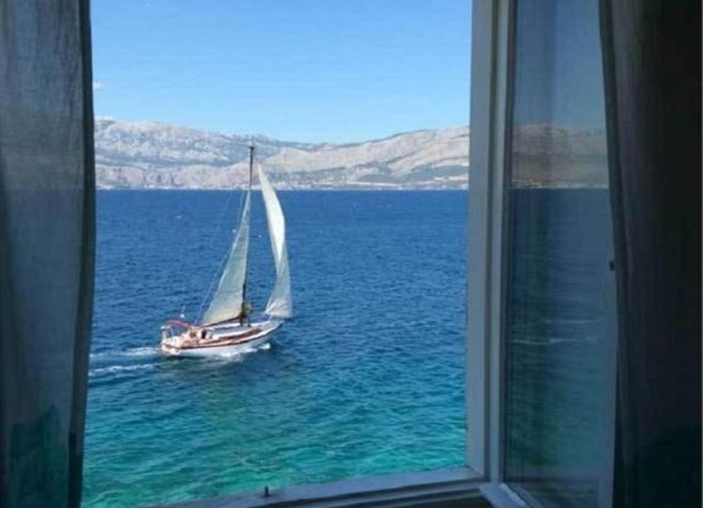 a sail boat in the water through a window at Apartment Sova - 20m from beach in Postira