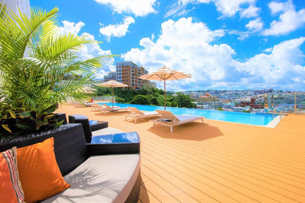 una terraza en la azotea con piscina, sillas y sombrillas en Novotel Okinawa Naha en Naha