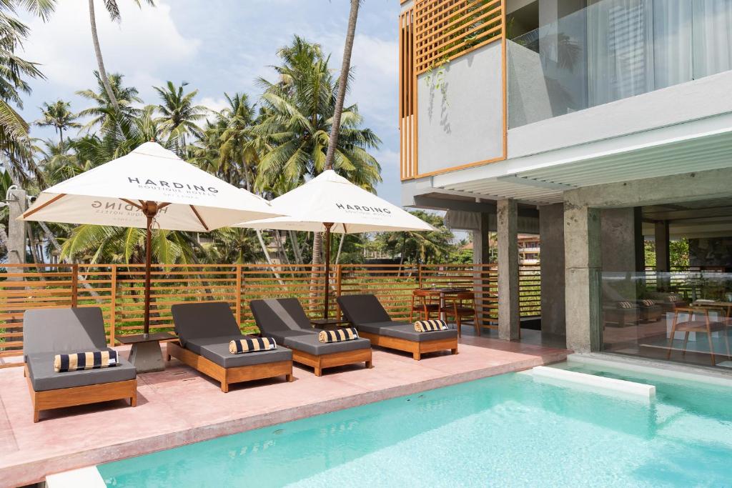 a pool with chairs and umbrellas next to a building at Harding Boutique Hotel in Ahangama