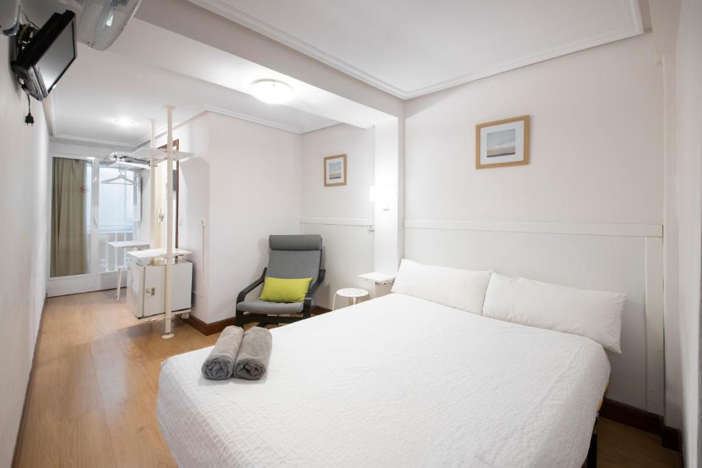 1 dormitorio con 1 cama blanca y 1 silla en Pensión Santa Clara, en San Sebastián