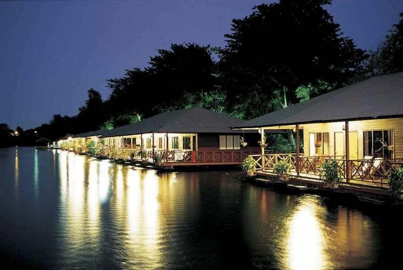 une rangée de maisons sur une rivière la nuit dans l'établissement Duenshine Resort, à Kanchanaburi