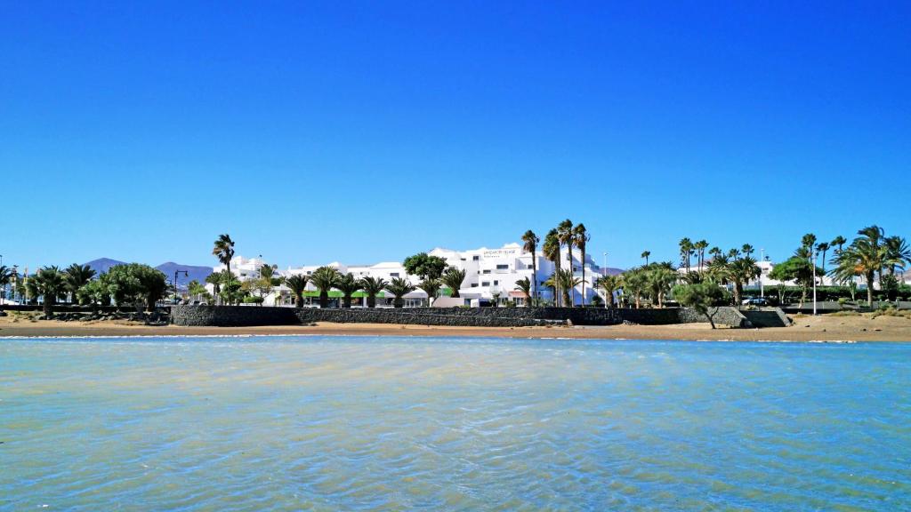 a view of a beach with palm trees and buildings at Hotel Lanzarote Village in Puerto del Carmen
