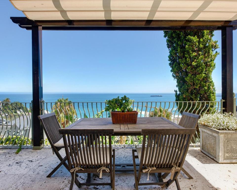 uma mesa de madeira com cadeiras e o oceano ao fundo em Villa del Mar - "Luxurious en-suite bedroom with lounge and stunning sea view balcony in Bantry Bay" em Cidade do Cabo
