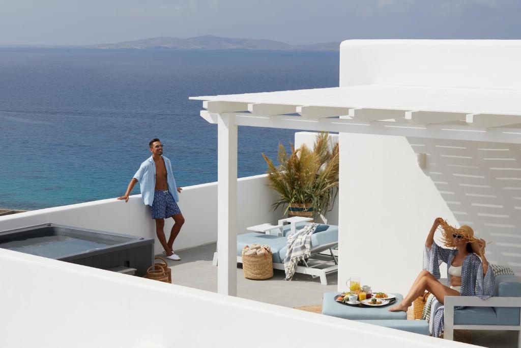 a man walking on a balcony with the ocean in the background at Epic Blue Mykonos in Houlakia
