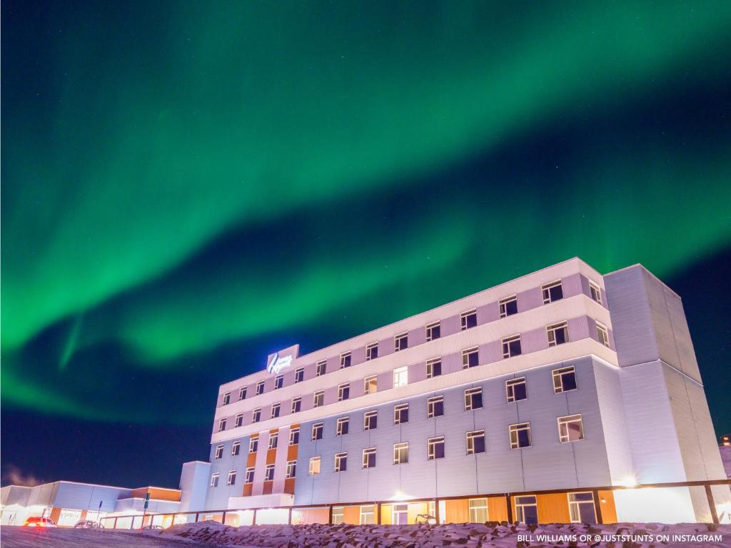 an office building with the green northern lights in the sky at Aqsarniit Hotel and Conference Centre in Iqaluit