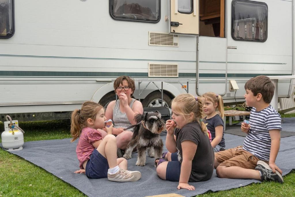 a group of children and a woman and a dog in front of a rv at Leithfield Beach Holiday Park in Leithfield