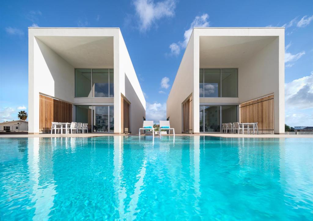 a swimming pool with blue water in front of two buildings at CARAIBAS Bonaire modern air-conditioned vacation home for architectural design lovers in Belnem