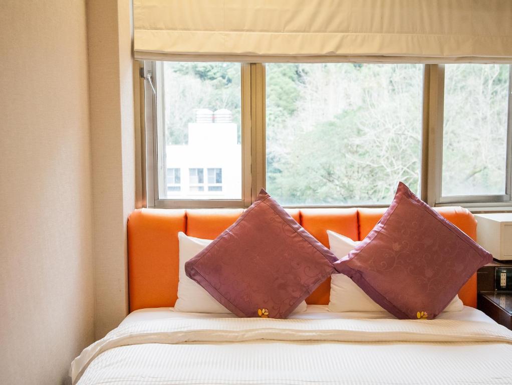 a bed with two pillows in front of a window at Mei Jia Mei Hotel in Jiaoxi