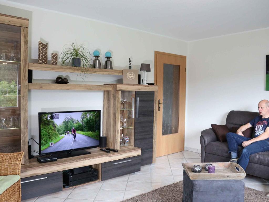 a man sitting on a couch in a living room with a television at Ferienwohnung Voege in Schmallenberg