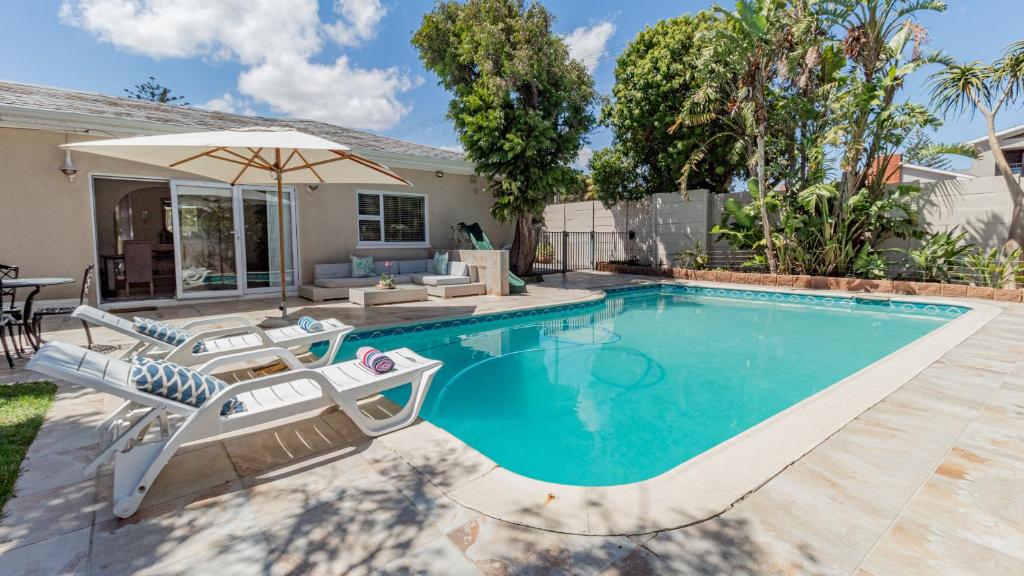 a swimming pool with chairs and an umbrella next to a house at Sea Breeze Guest House in Bloubergstrand