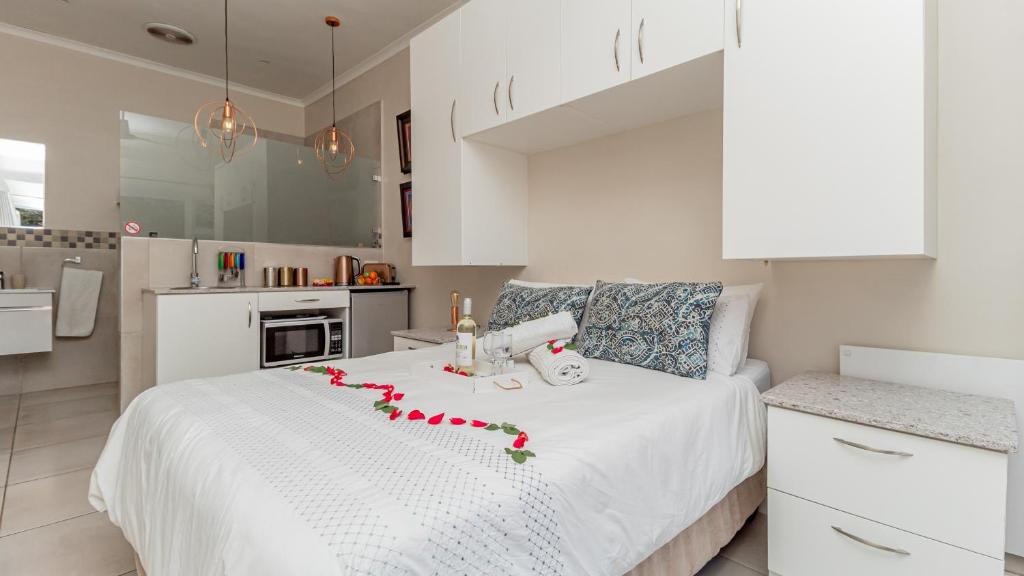 a white bedroom with a white bed with red flowers on it at Sea Breeze in Bloubergstrand