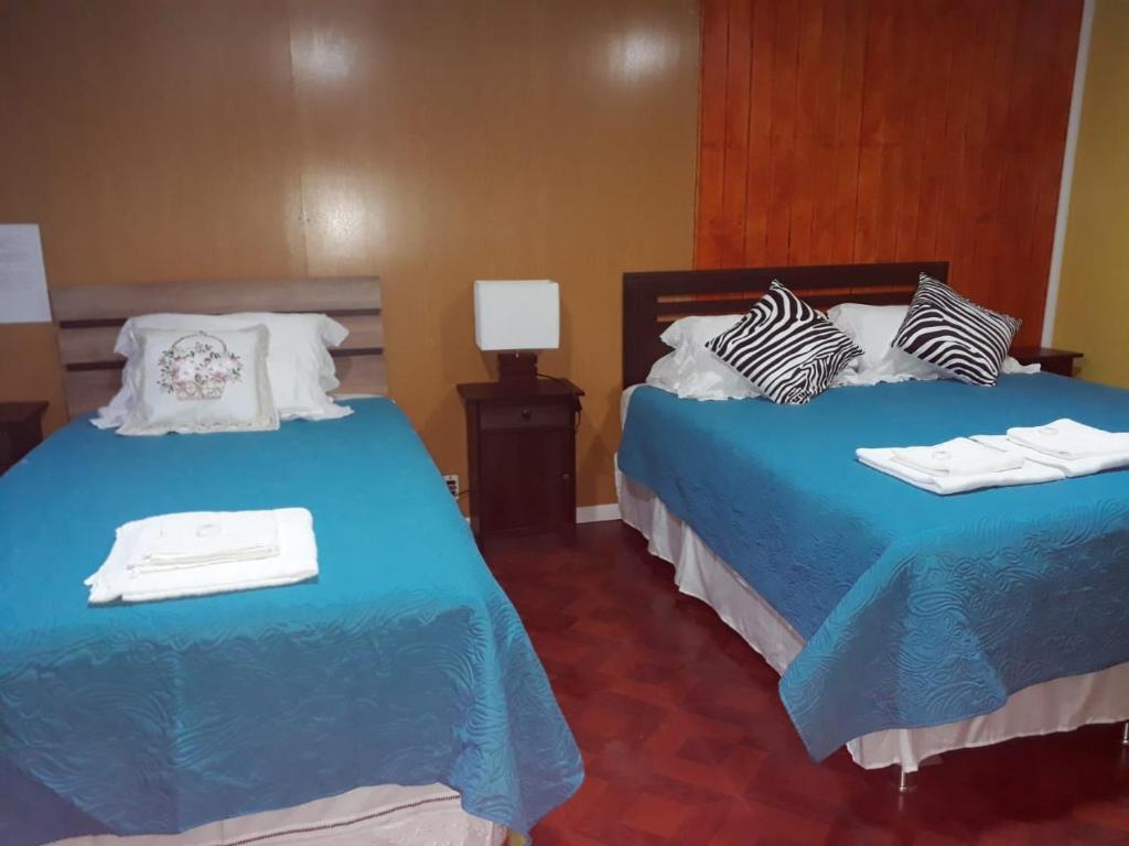 1 dormitorio con 2 camas con sábanas y almohadas azules en hostal geminis ,phillipi 653 centro en Puerto Natales