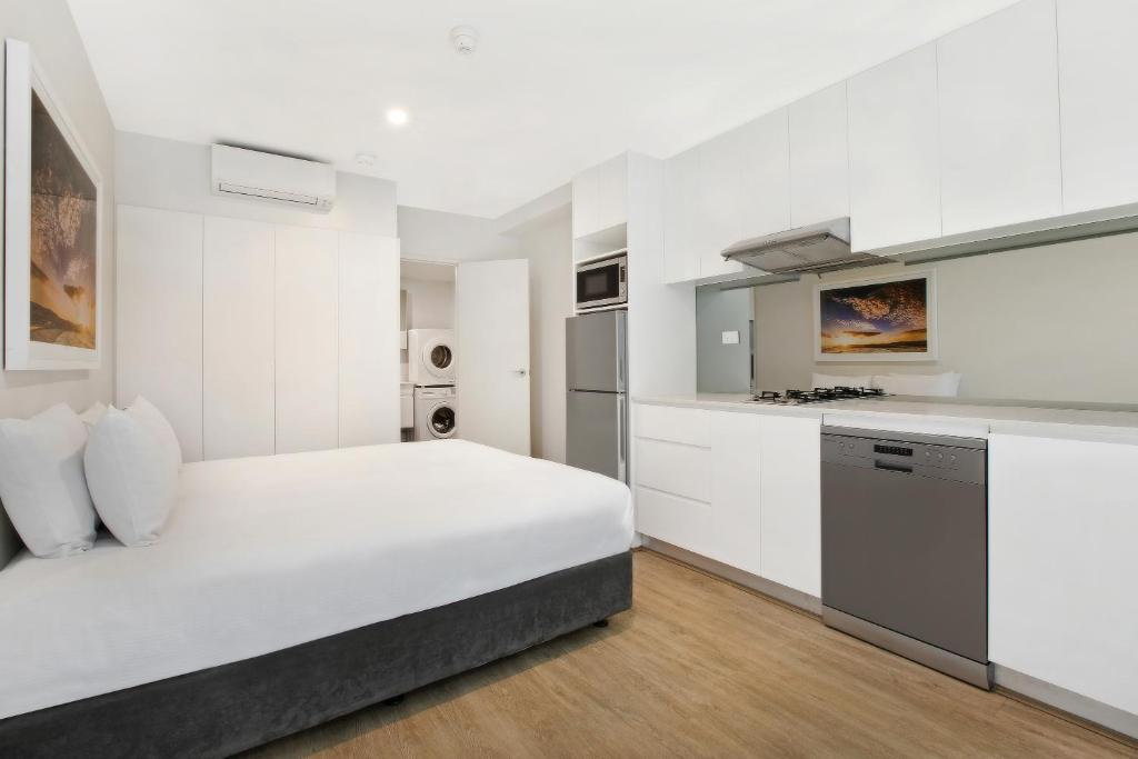 a white bedroom with a large bed and a kitchen at Bondi Beach Studios Suite in Sydney