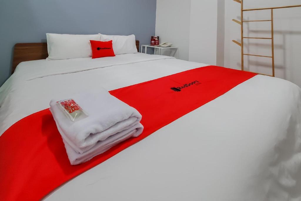 RedDoorz Plus @ Batutulis Bogor في بوغور: سرير ابيض وفوط حمراء وبيضاء عليه
