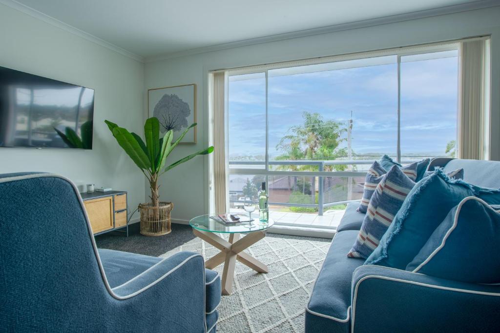 una sala de estar con muebles azules y una gran ventana. en Top Of The Quays, en Merimbula