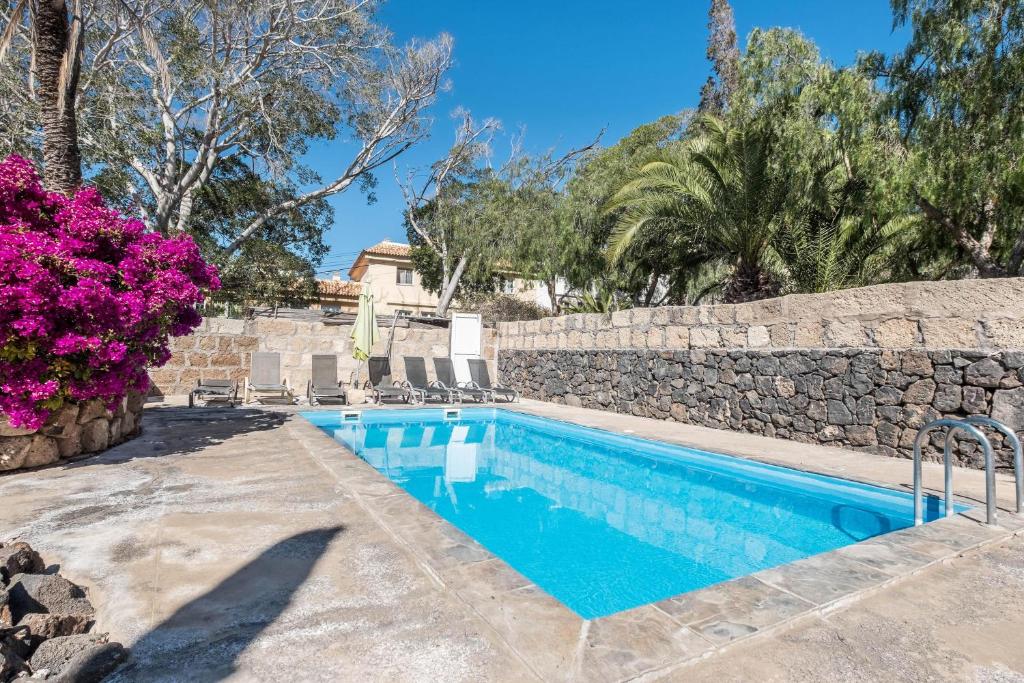 a swimming pool with a stone wall and purple flowers at Flamboyán in Adeje