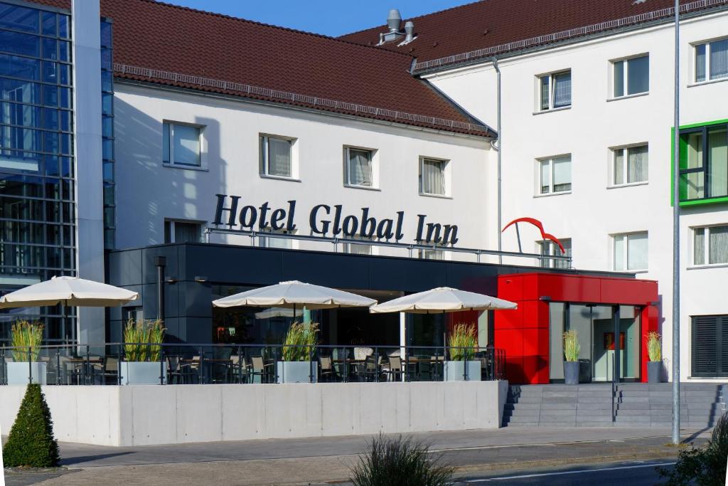 een hotel met tafels en parasols voor een gebouw bij Hotel Global Inn in Wolfsburg