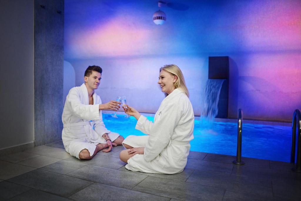 Un uomo e una donna seduti sul pavimento di fronte a una piscina di Hotel Fado Spa & Restaurant a Świdnica