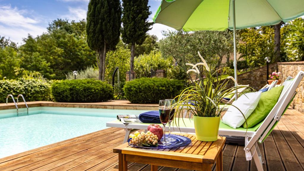 a table with a glass of wine and an umbrella next to a pool at TENUTA DI MACERICCA 10, Emma Villas in Poggibonsi